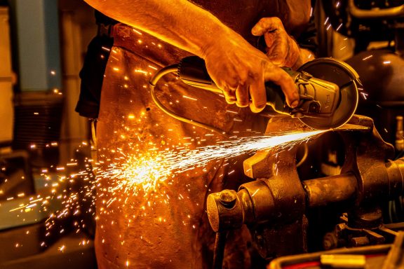 Une main utilise une meuleuse, produisant des étincelles dans un environnement industriel.